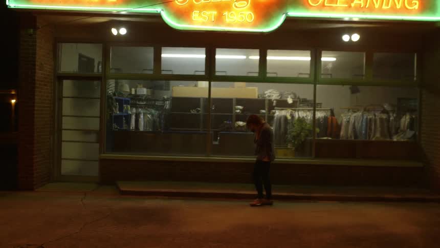 A woman paces outside a laundromat at night