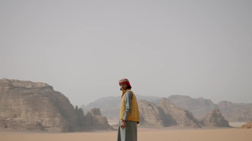 A man wearing a turban looks around in the desert