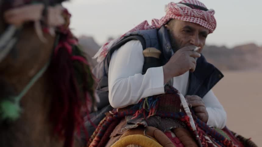 A man smokes a cigarette on the back of a camel