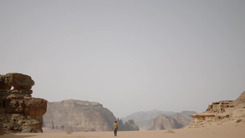 An arab man is walking alone in a desert landscape
