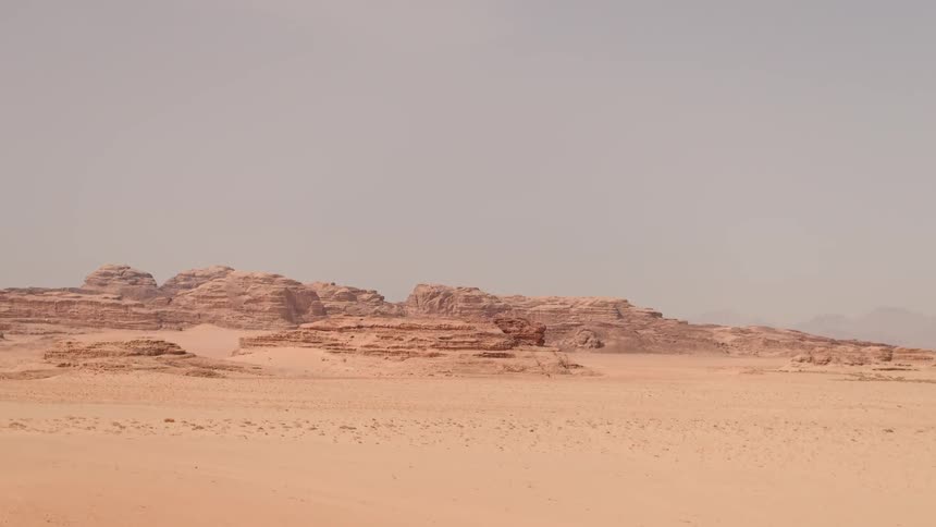 Mountains surrounded by sand sit under a blue sky