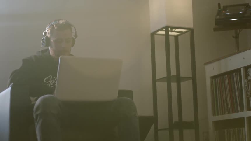 A man is sitting on a chair with his laptop and headphones