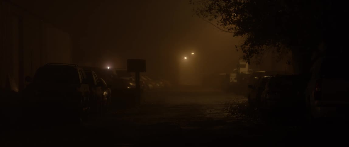 Lamp posts illuminate the hazy parking lot