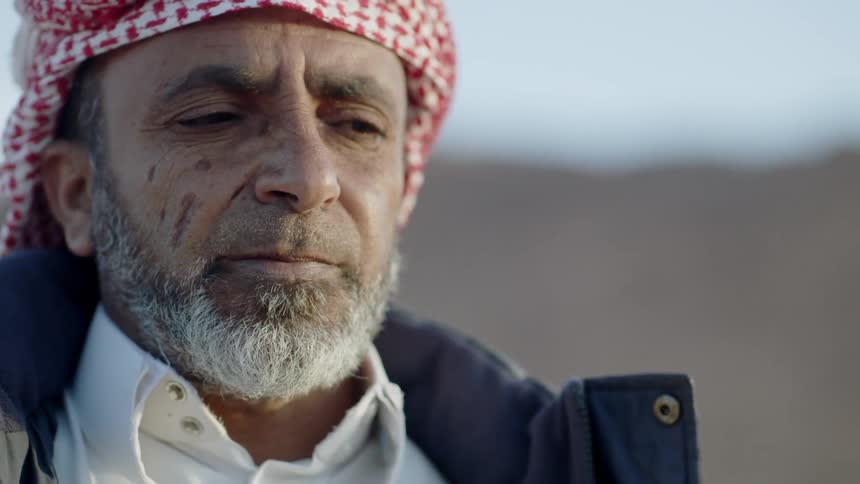 An old arab man is standing in the desert