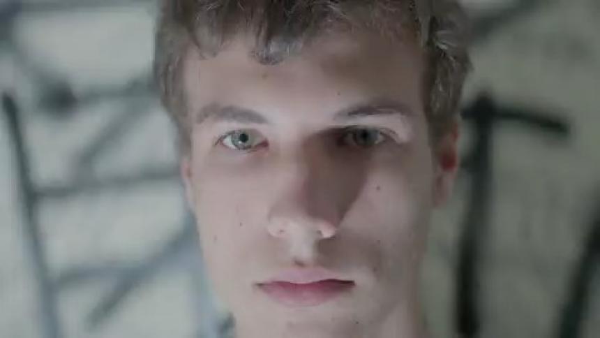 A man in a dark room stares at the camera while a strobe light is flashing
