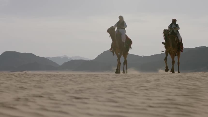 Two people ride camels in the desert