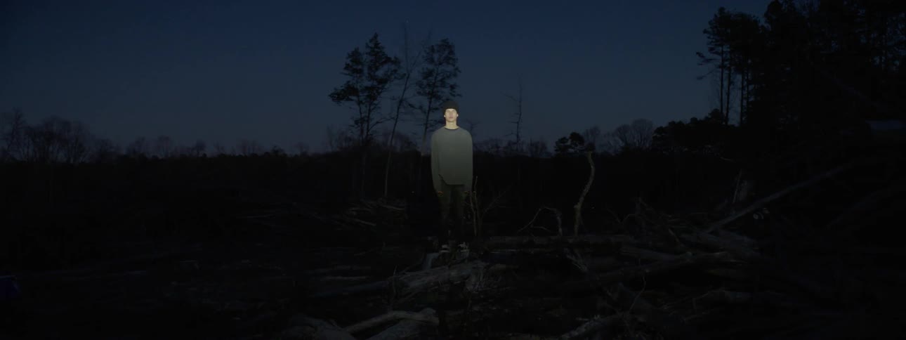 A young man is standing in a field with a flashing light shining on him
