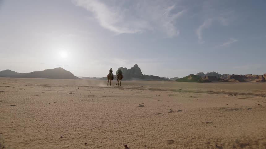 Two people ride camels in the desert
