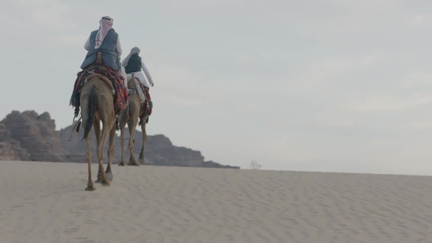 Two people ride on camels in the desert