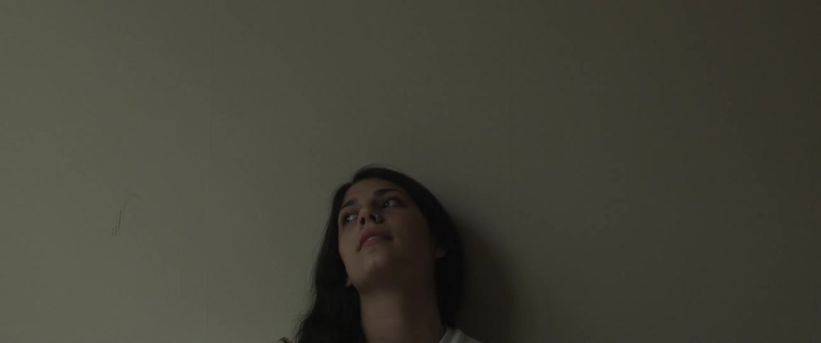 A woman leans against a wall looking up