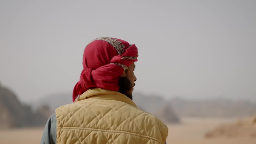 A man with a scarf on his head stands in a desert
