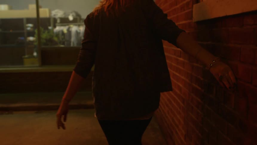 A walking woman runs her hand along a brick wall