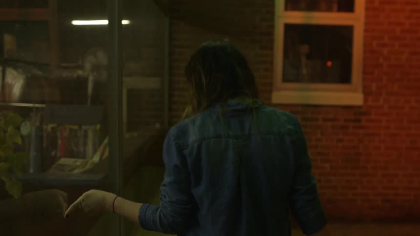 A woman is walking down the sidewalk running her finger along a window