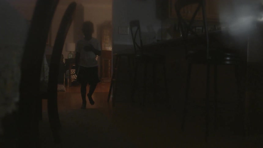 A boy holds his hand to his chest as he walks through his home at night