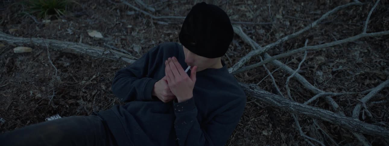 A young man is sitting in the woods and smoking