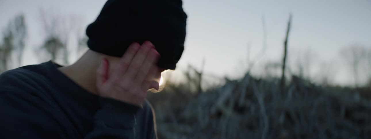 A teenager removes a ski mask from his face and slaps himself