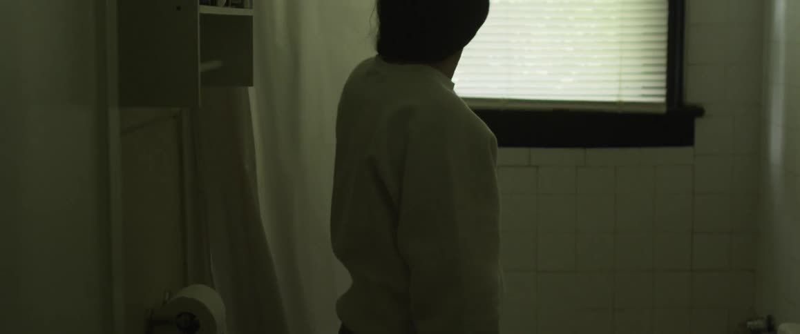 A woman is sitting on the edge of a tub and she gets up and closes the shower curtain