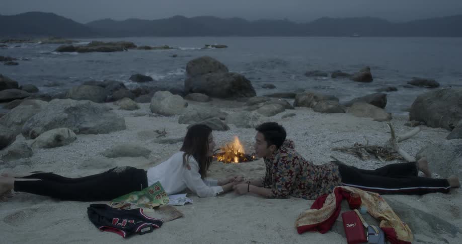 A couple talk by a campfire near the shore