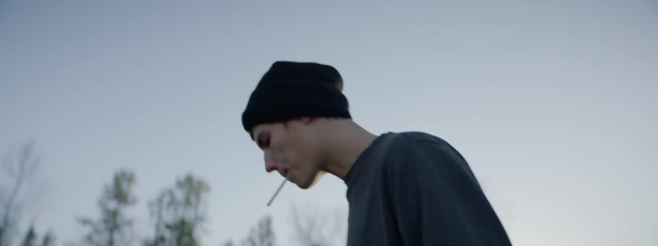 A man in a beanie lights a cigarette
