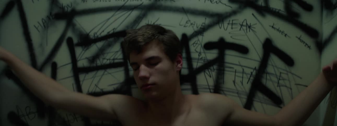A young man is lying and rubbing against a wall with graffiti with a strobe light flashing