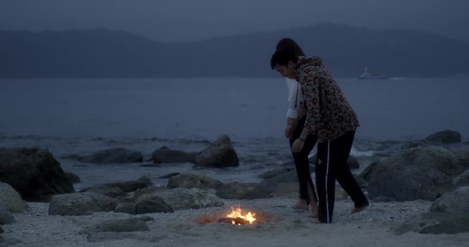 A man and woman run around a beach campfire