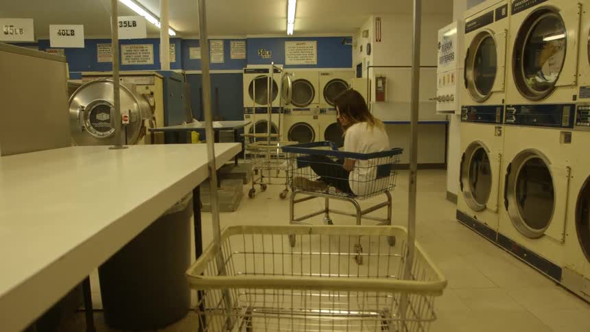 A woman sits in a laundromat basket