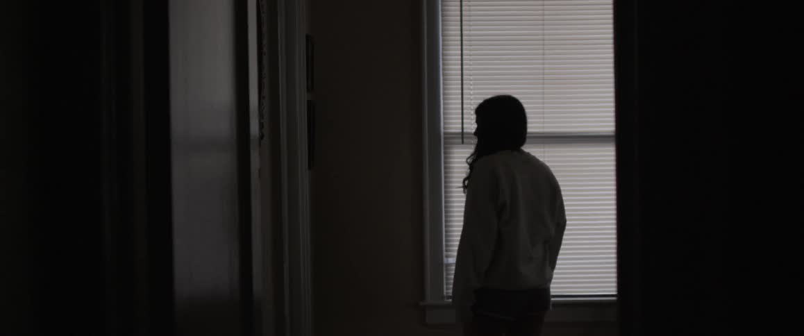 A girl walks towards a window and looks around at her surroundings