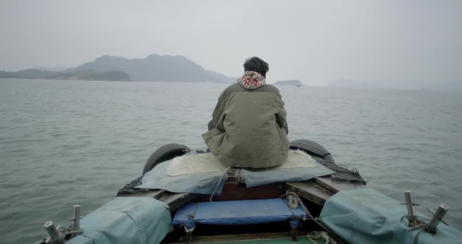 A man sits on the front of a makeshift raft and travels on the water