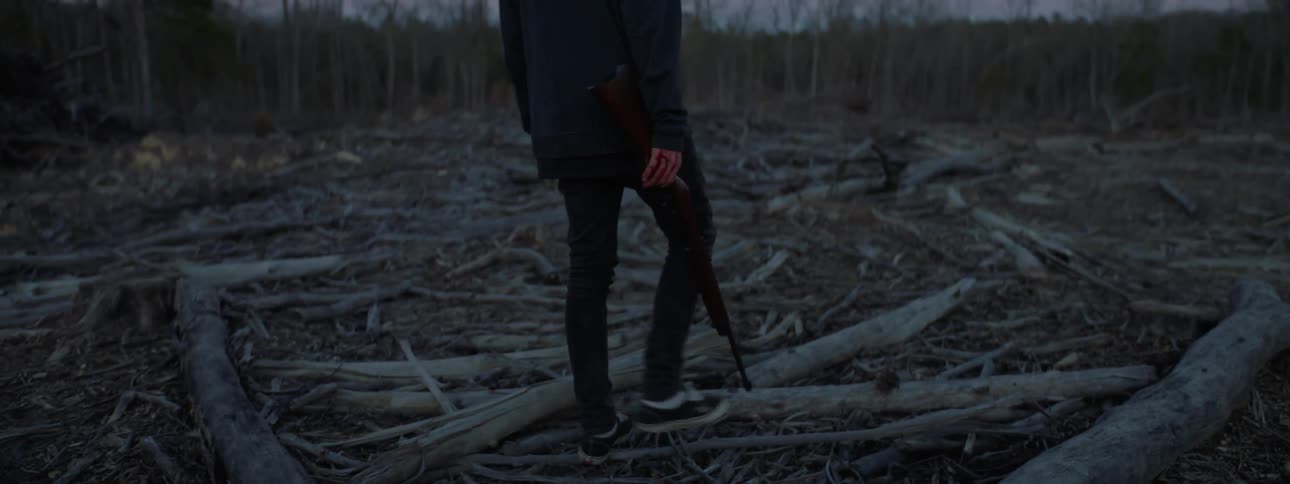 A man carries a rifle in the woods