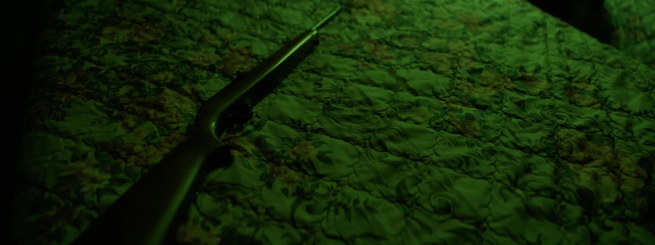 A rifle is laying on the bed in the dark room