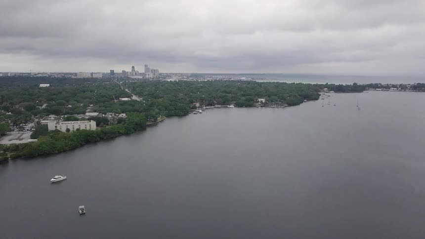 Sailboats are anchored off the coast with a city skyline in the distance
