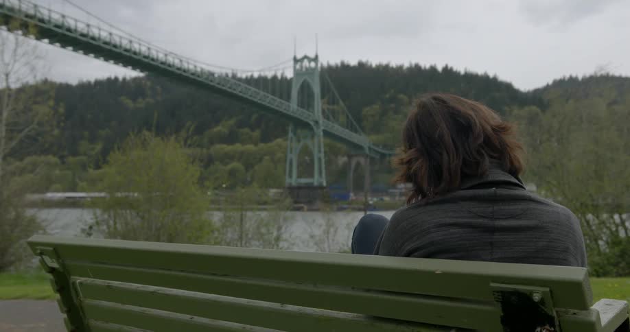 A lonely woman sitting on a bench by the bridge