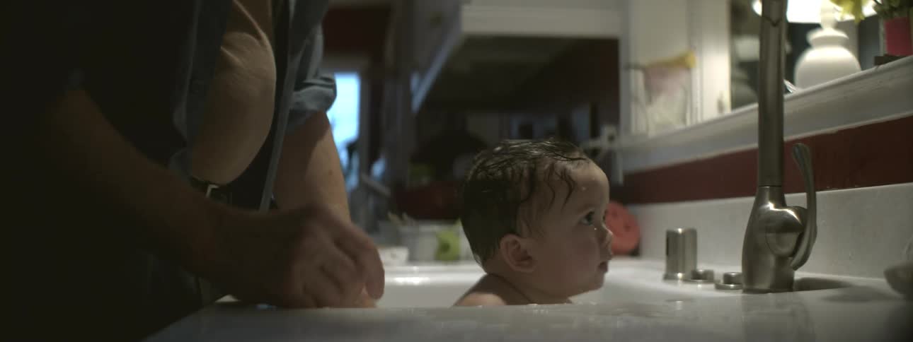 A baby is being given a bath in the kitchen sink