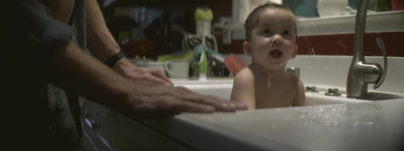A parent is bathing a baby in the kitchen sink