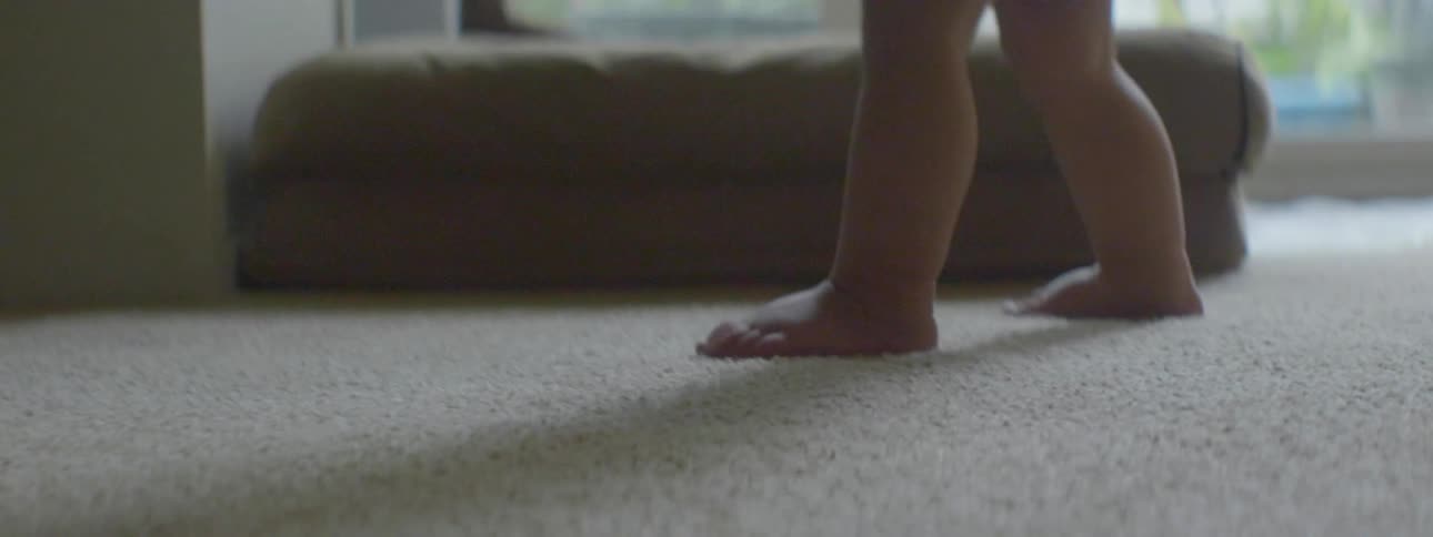 A baby walks on a carpeted floor