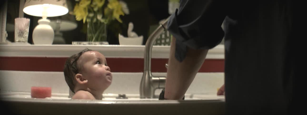 A man is giving a baby a bath in a kitchen sink