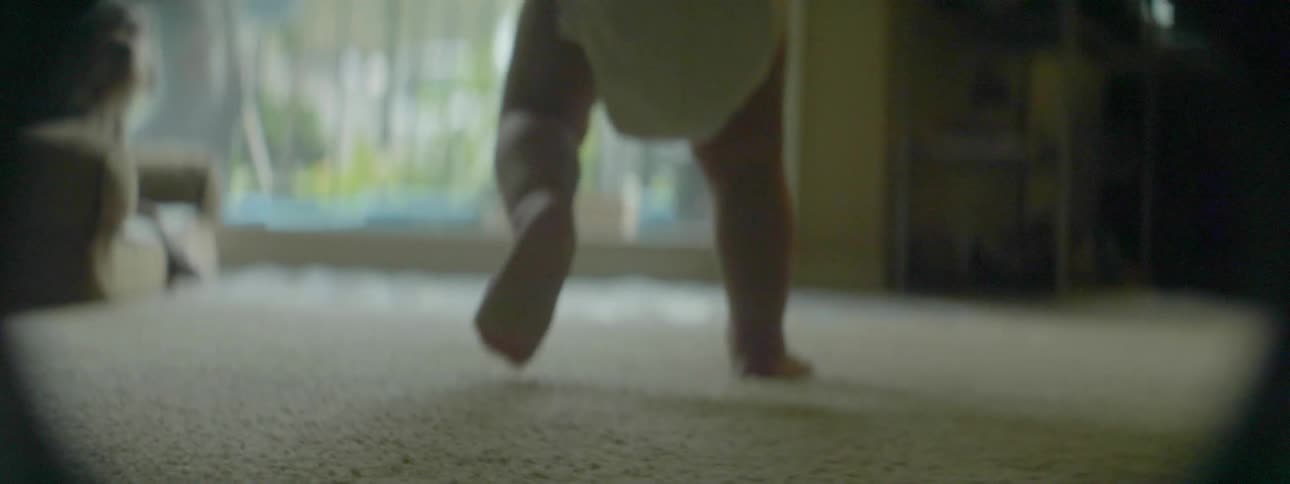 A baby is walking in a living room toward a sliding glass door