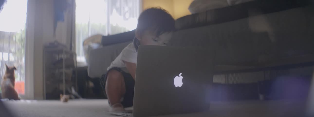 A baby sits on the floor with a laptop