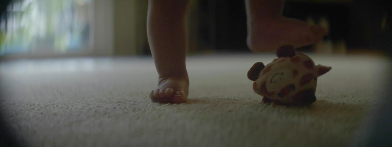 A baby is walking to a toy and stepping on it in a living room