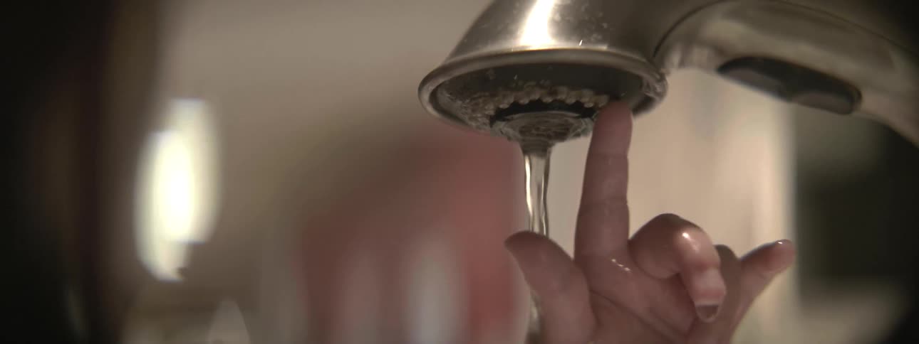 A baby puts his hand up to a faucet