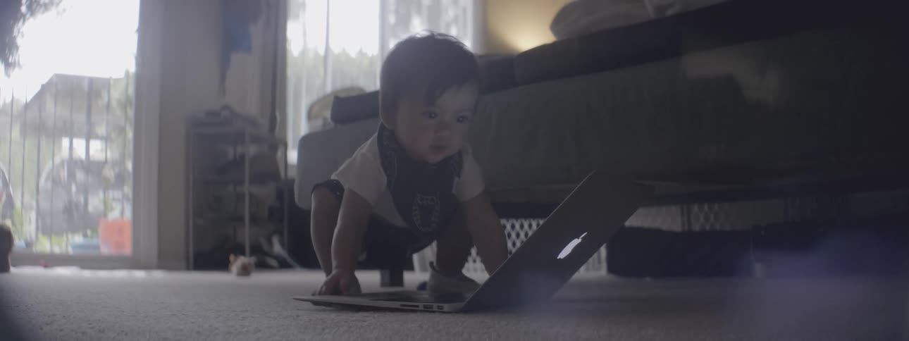 A baby plays on the floor with a laptop