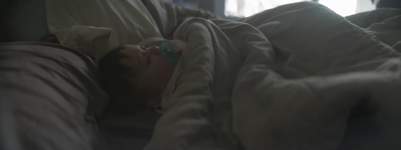 A baby is sleeping under the covers on a bed
