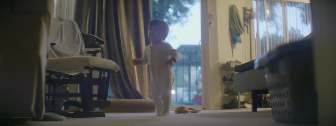 A baby is walking in the living room swinging a toy