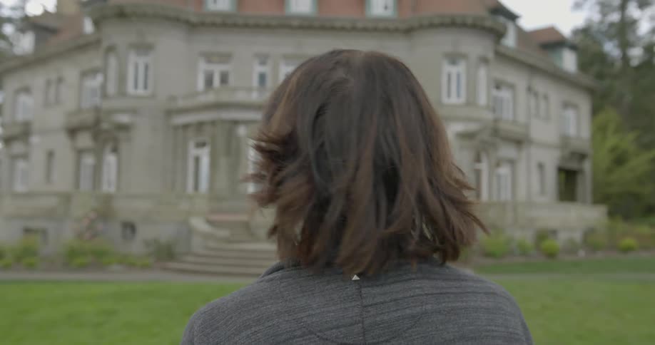 A woman walks towards a large house