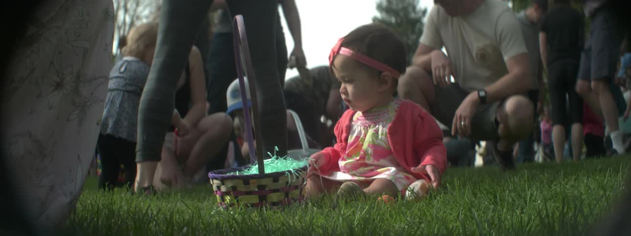 A baby plays with easter eggs in front of a crowd