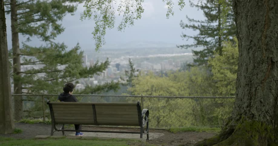Someone sits on a bench overlooking a skyline with mountains in the distance