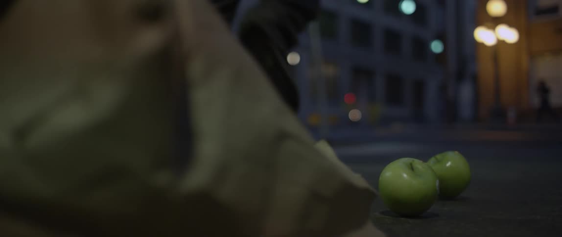 Apples falling out of a sack onto a city street as a person runs away