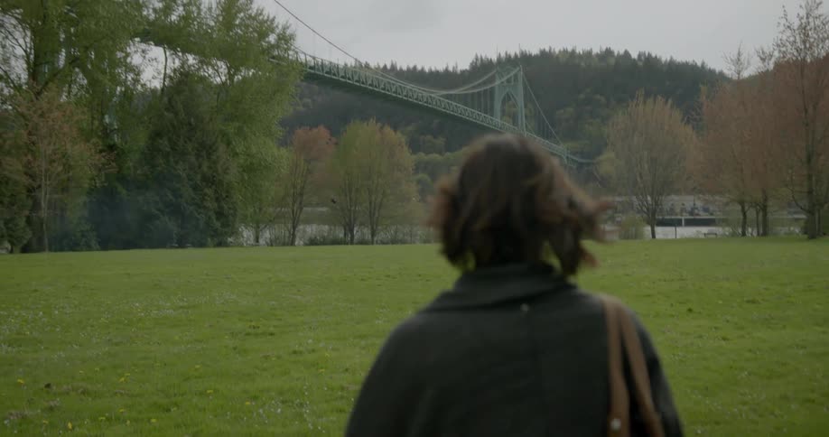 Woman walking across a field with a bridge in the background