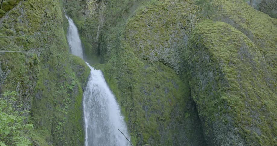 A waterfall rushes over green stone cliffs during the day