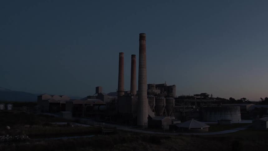 Smoke stacks in a factory stand against a dusk sky